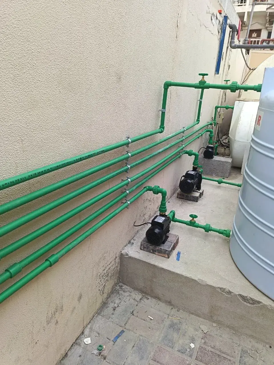 Green PPR water supply pipes and booster pumps next to a water tank